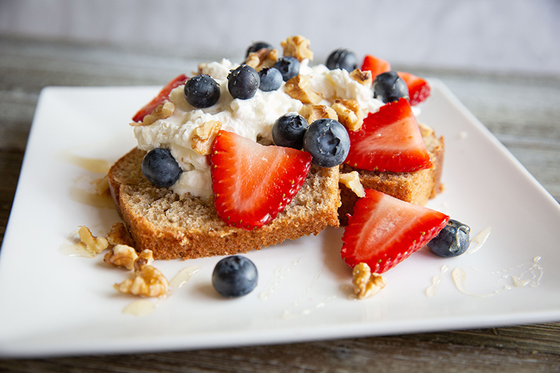 Banana Bread Stacked with Homemade Whip and Berries on White Plate.