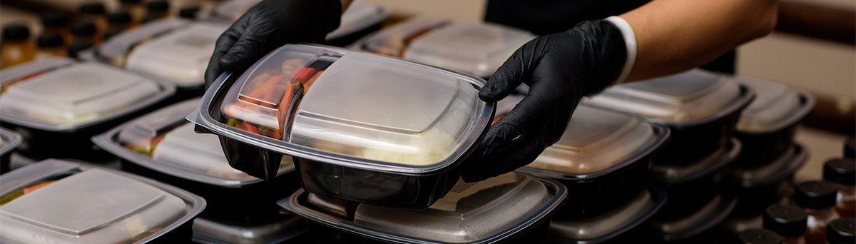 Hands with gloves putting food in plastic to-go containers for customers to pickup.